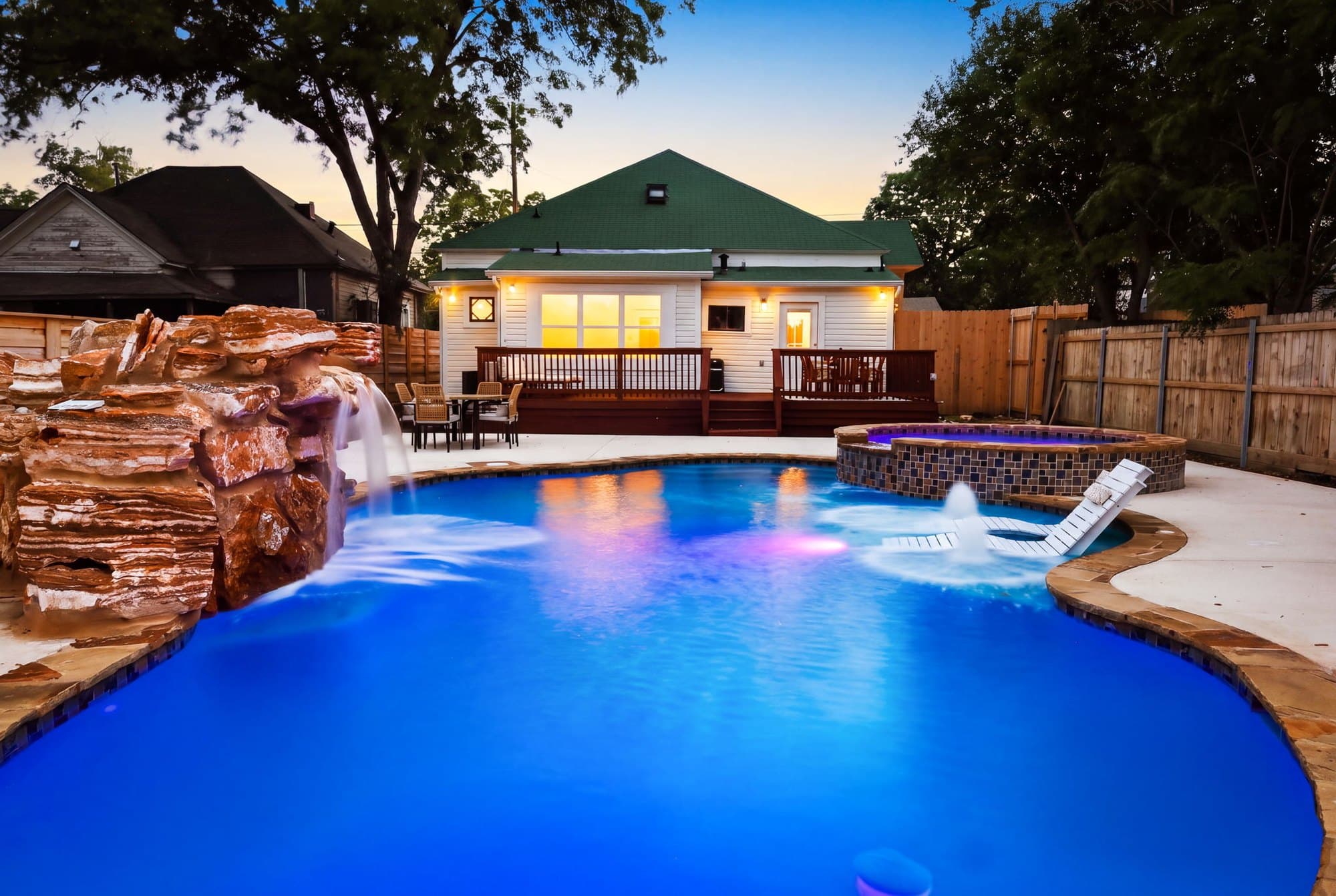 Rock waterfall and spa lit at dusk beside the pool