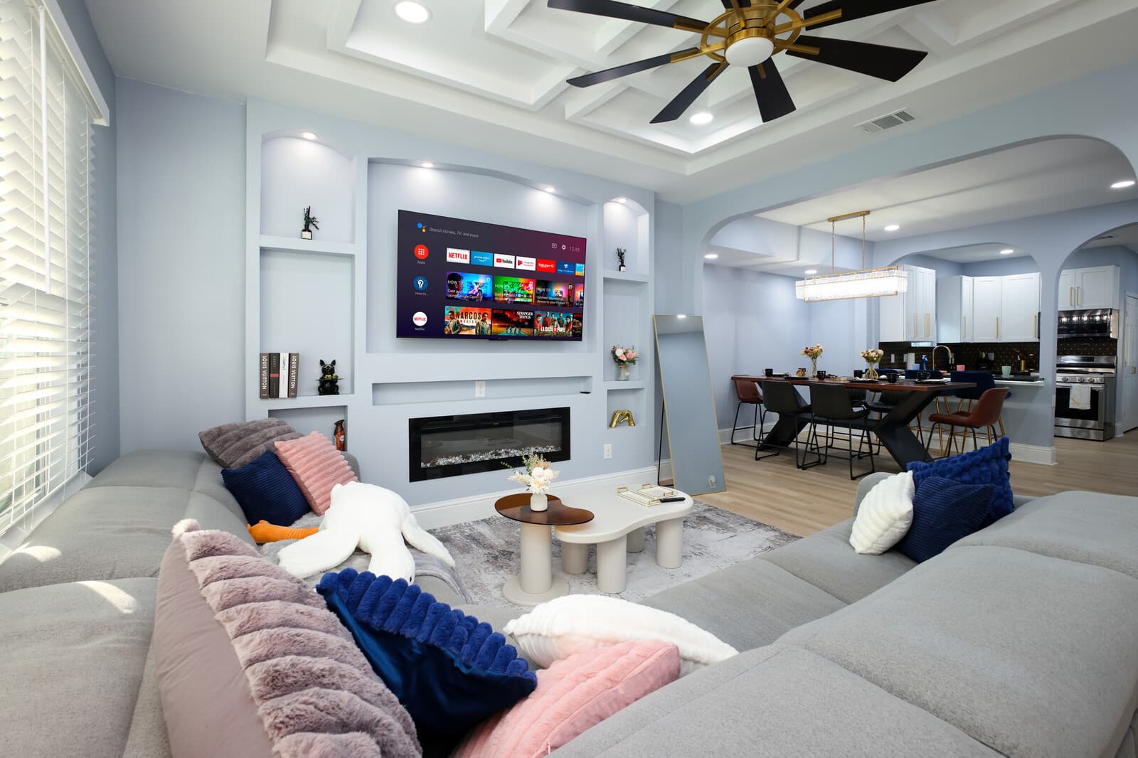 Open living room with a linear fireplace, mounted television and coffered ceiling detail