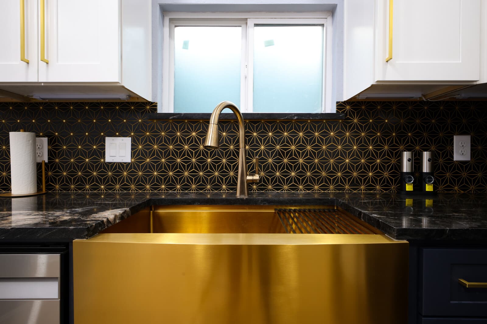 Brass farmhouse sink set against the dark patterned backsplash in the main kitchen